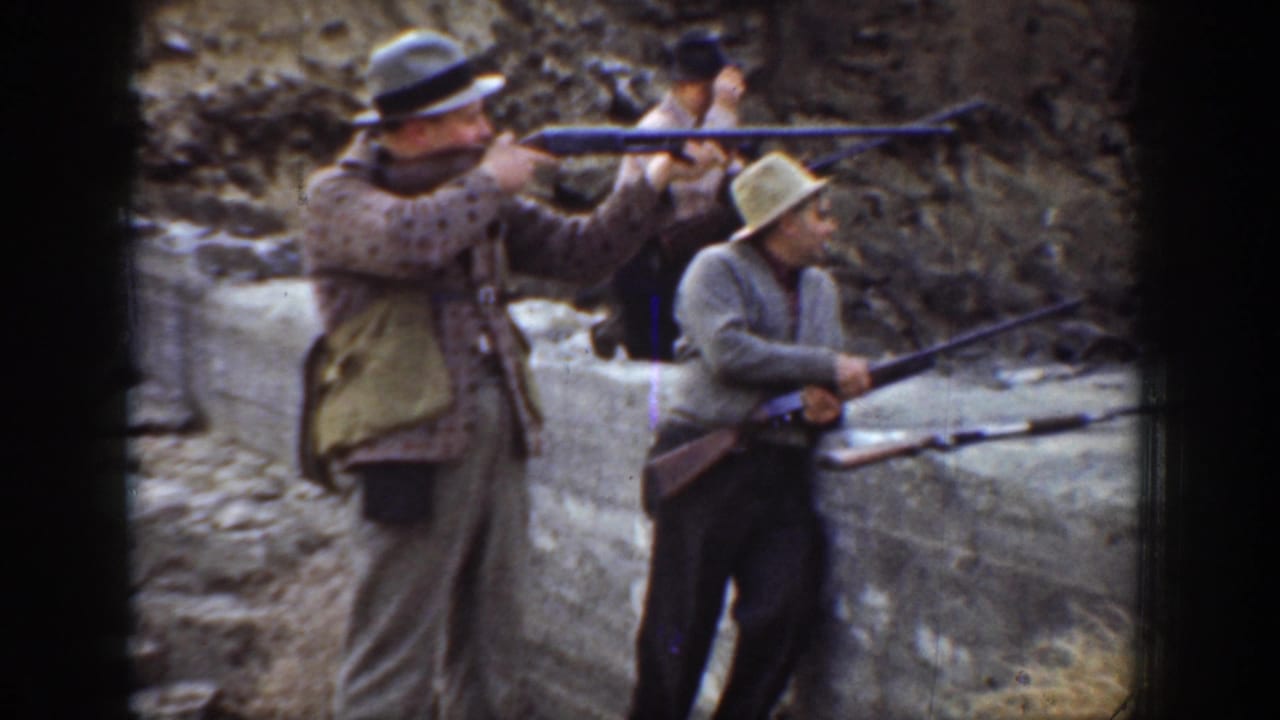 1936 California home-movie frame showing men in period hats aiming long rifles behind a concrete wall at an outdoor range.