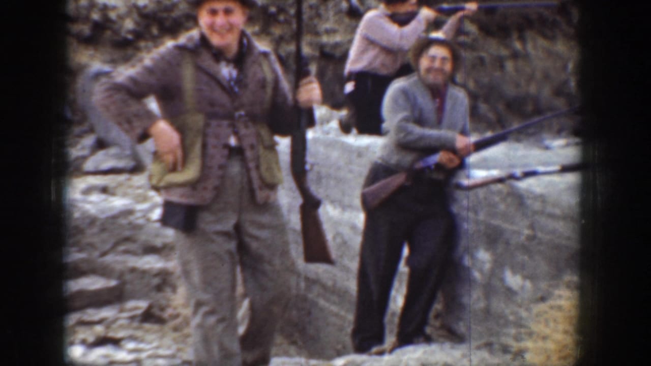 1936 California home-movie frame of men in casual period clothing posing with shotguns in a rocky dry landscape.