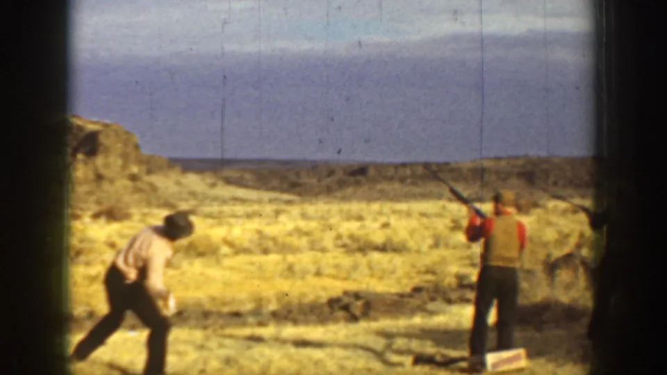 A man prepares near the ground while another aims a shotgun across an open California landscape in the supplied 1936 clip.