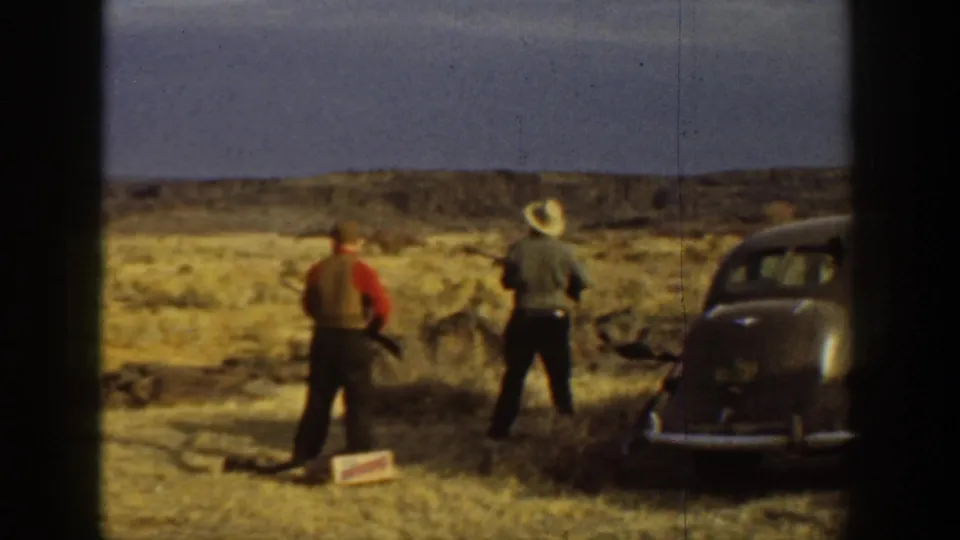 Two men with shotguns stand near a dark classic car in a dry California landscape in the supplied 1936 footage.