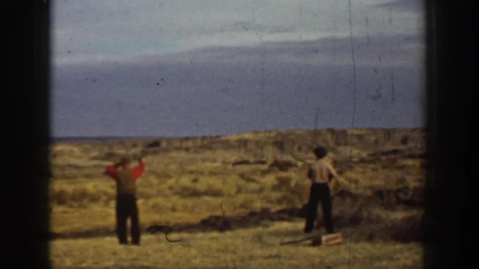 1936 California 8mm frame showing two men in a dry field, one in red and one in a light shirt and hat, during target practice.