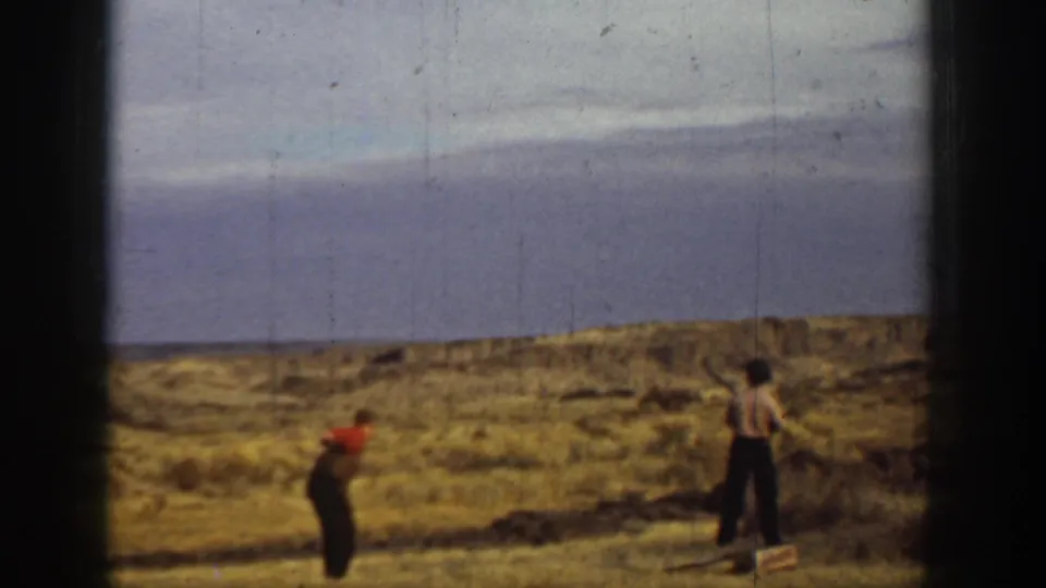 1936 California 8mm frame showing two men in a dry California field, one bending near the ground and the other holding a long object.