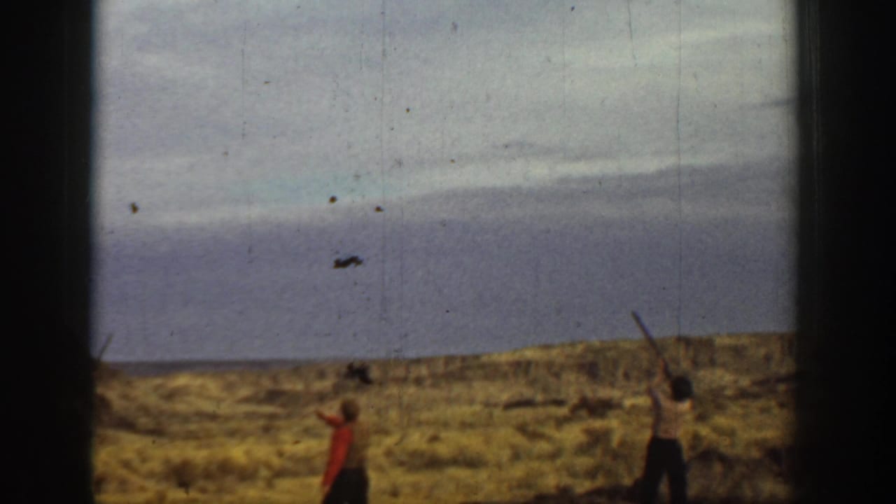In 1936 California home-movie footage, three men appear in a dry open field during shotgun practice, partly obscured by contact-sheet borders.