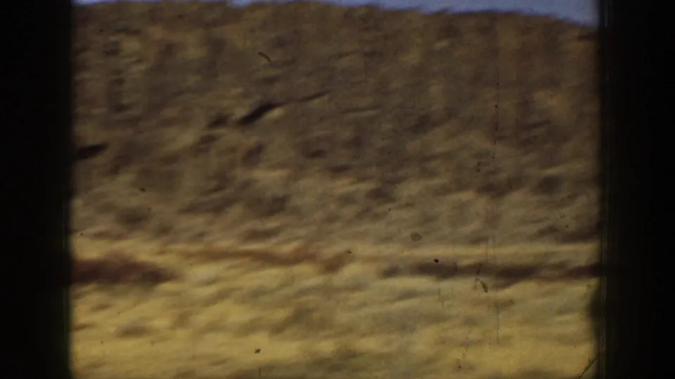Soft, blurred 8mm frame of the arid field and hillside at the end of the California target-shooting clip.
