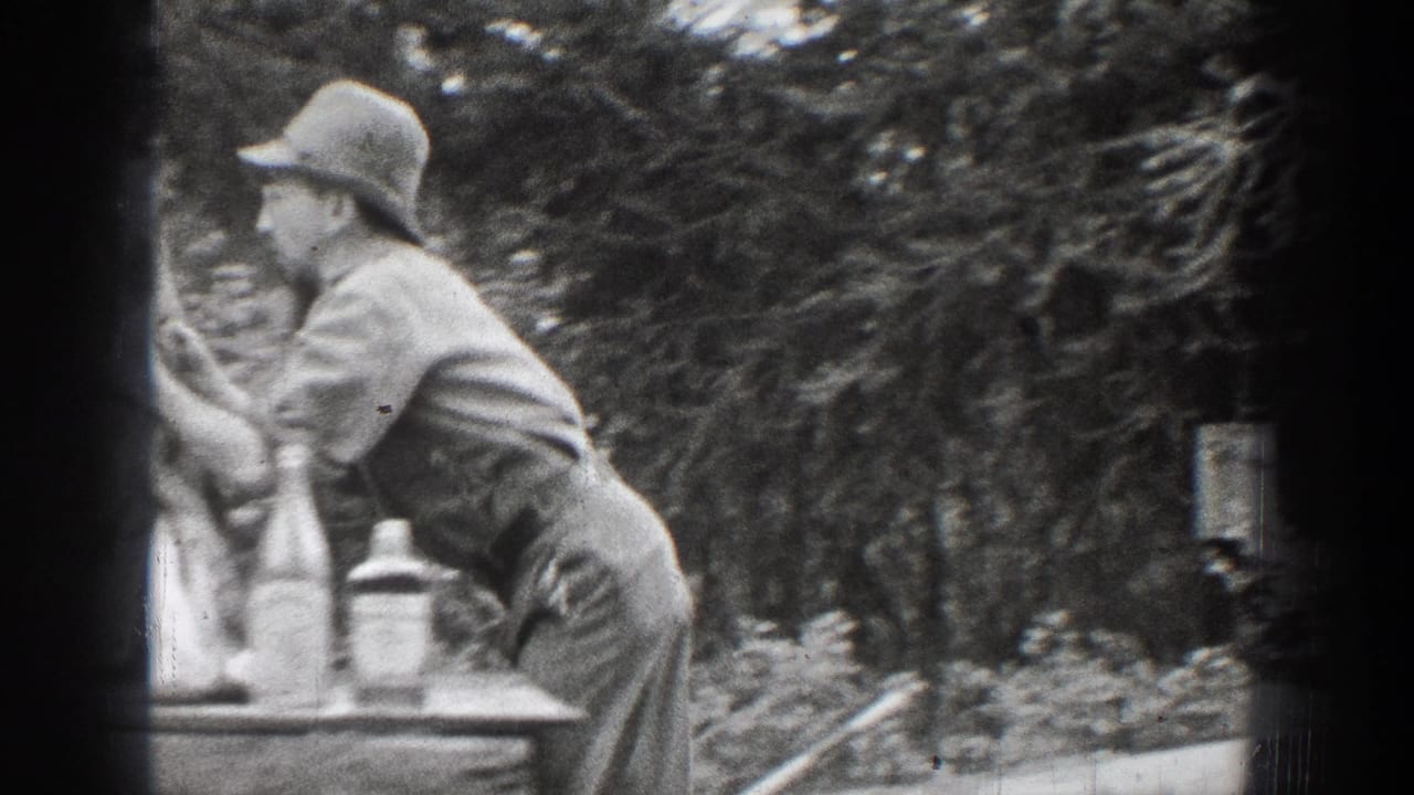 The man appears in profile, leaning toward the deer head on or near a table in the wooded Chelan home-movie scene.