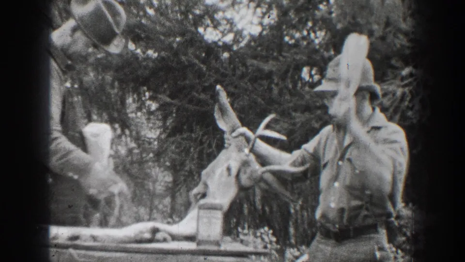 1939 Chelan-area home-movie frame showing men in hats near a deer in a wooded outdoor setting.