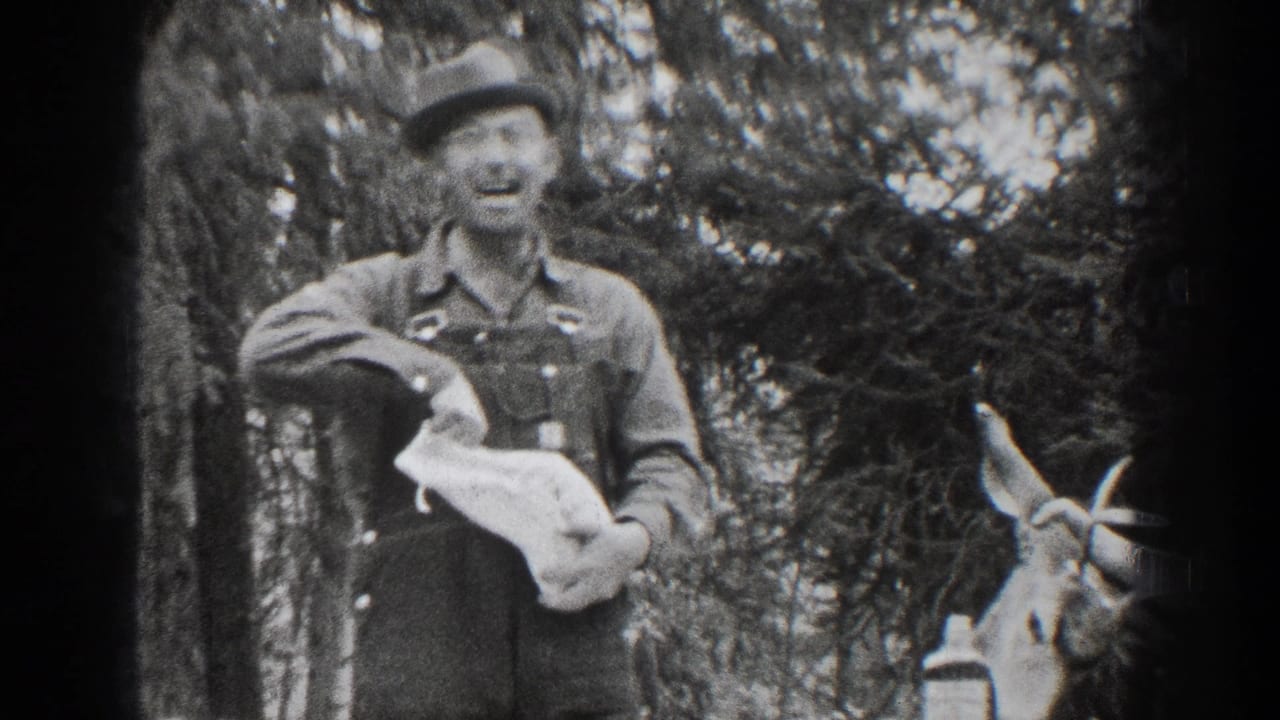 A smiling man in overalls faces the camera in wooded 1939 Chelan footage, with a deer at the right edge.