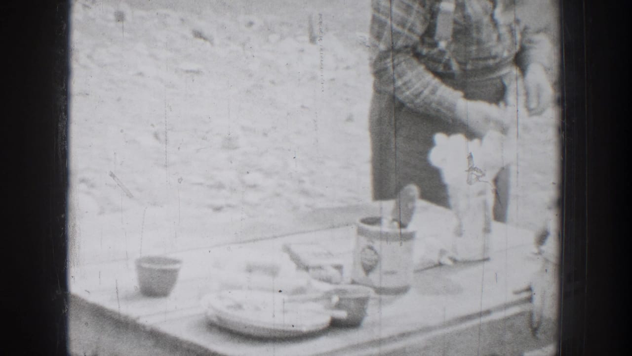 1939 Chelan, Washington home-movie frame showing a camp table with dishes, tins, and a man partly visible beside outdoor meal supplies.