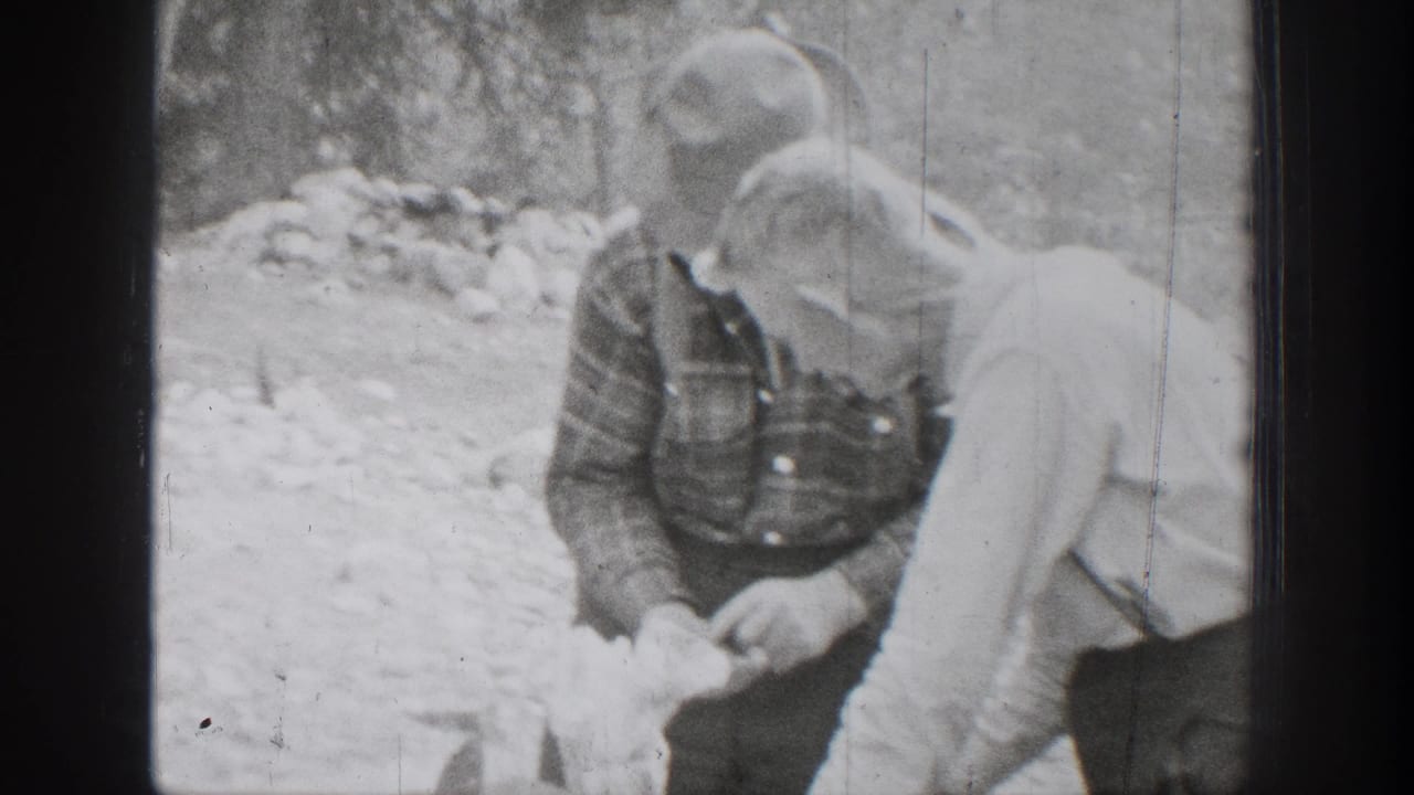 1939 Chelan, Washington frame showing two hunters in brimmed hats and work clothes handling food during a forest meal preparation.