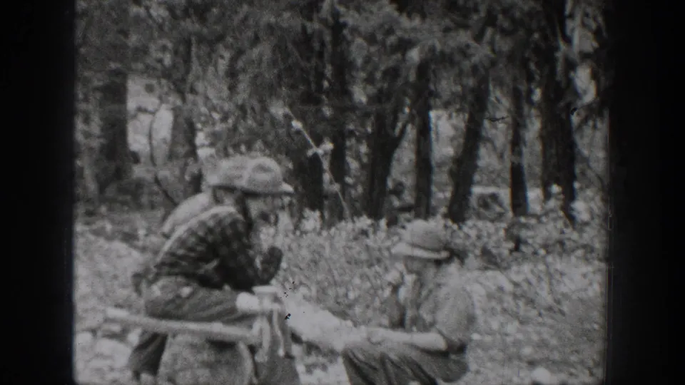 1939 Chelan, Washington home-movie frame with seated and leaning men gathered in a wooded hunting camp setting.