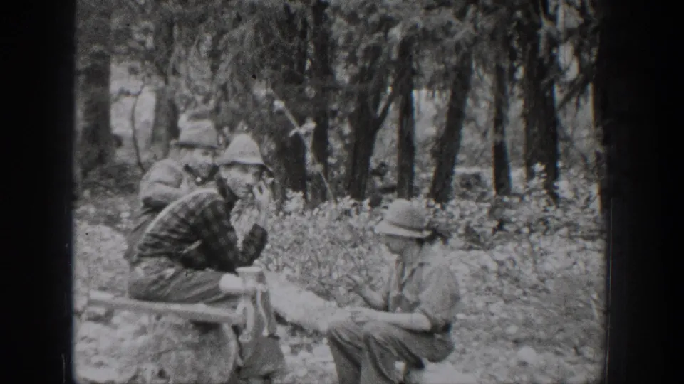 1939 Chelan, Washington frame showing men in hats gathered around a low camp table or bench in the forest.