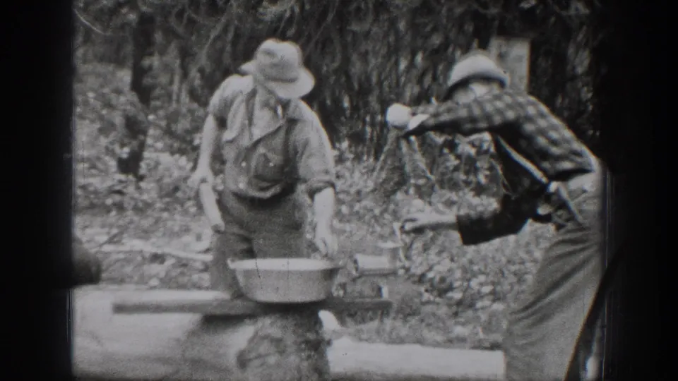 Chelan, Washington 1939 frame with one man handling a metal basin as another man in a plaid shirt reaches toward the outdoor work surface.