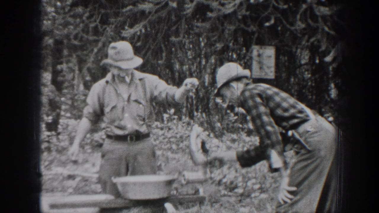 A man stands by a basin while another bends forward in the woods.