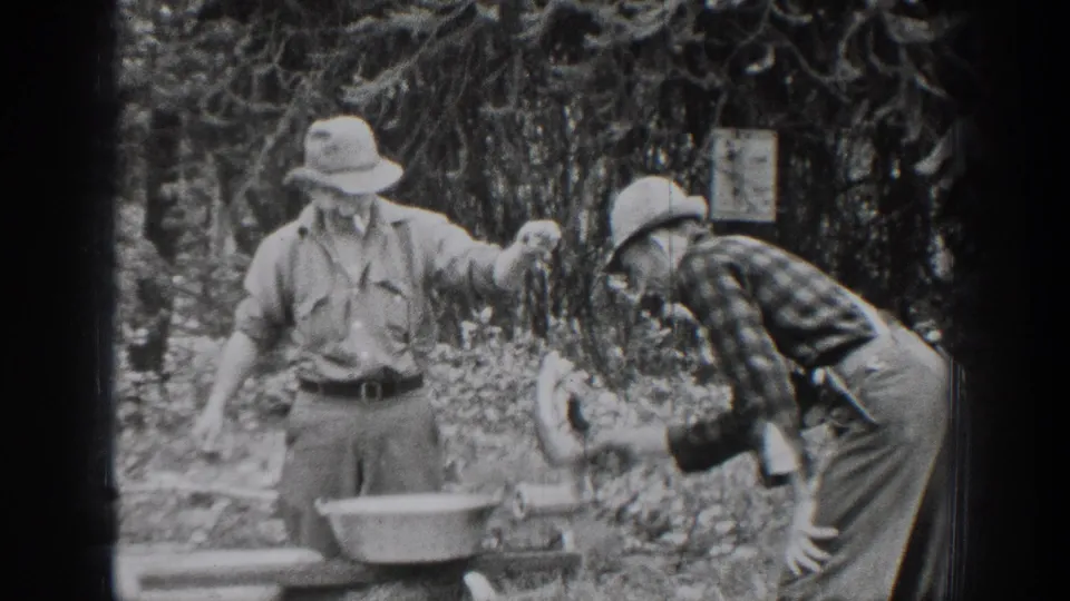Two adult men in hats work near a basin in a wooded Chelan, Washington setting, with one bending over equipment.