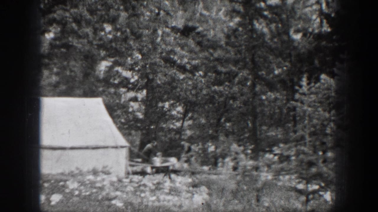 1939 Chelan, Washington camp scene with a white canvas tent and a man working near a small table in dense woods.