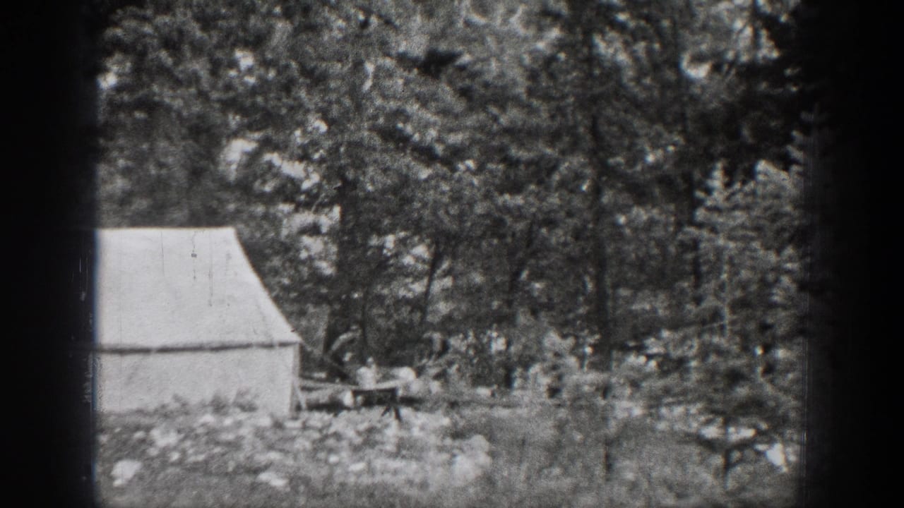 1939 Chelan, Washington frame showing a man near a table and white canvas tent within a shaded forest campsite.