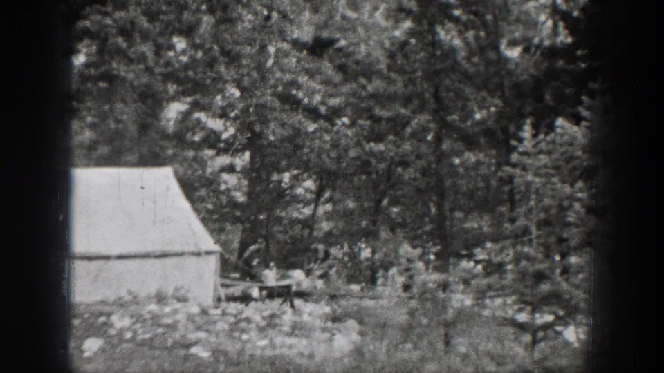 1939 Chelan, Washington frame showing a man near a table and white canvas tent within a shaded forest campsite.
