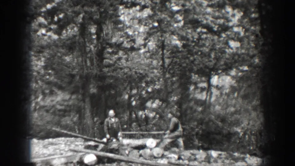 1939 Chelan frame with two men beside logs or lumber, one handling a long saw in a forest campsite setting.