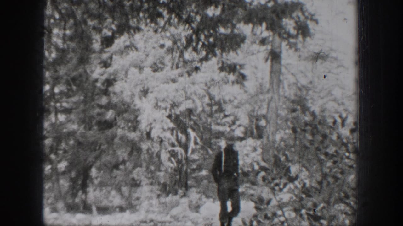 1939 Chelan home-movie frame showing a man walking through a wooded area with dense branches and soft black-and-white exposure.