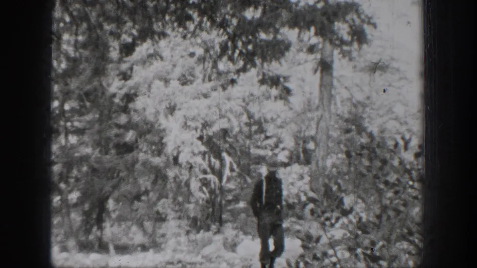 1939 Chelan home-movie frame showing a man walking through a wooded area with dense branches and soft black-and-white exposure.