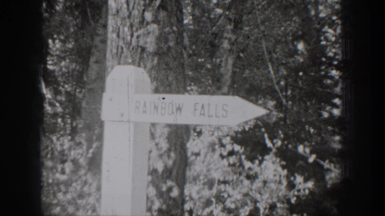A white Rainbow Falls signpost stands among trees in black-and-white 1939 Chelan footage.