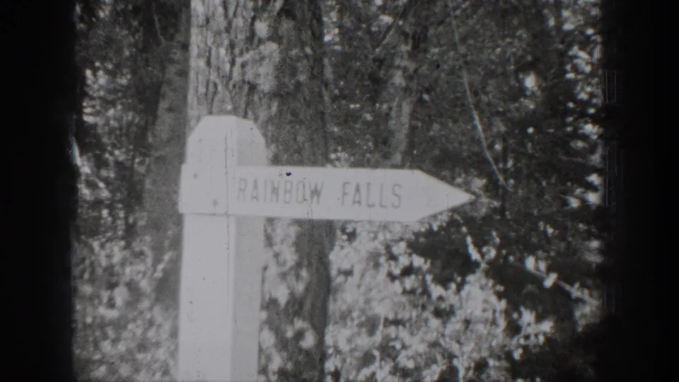A white Rainbow Falls signpost stands among trees in black-and-white 1939 Chelan footage.