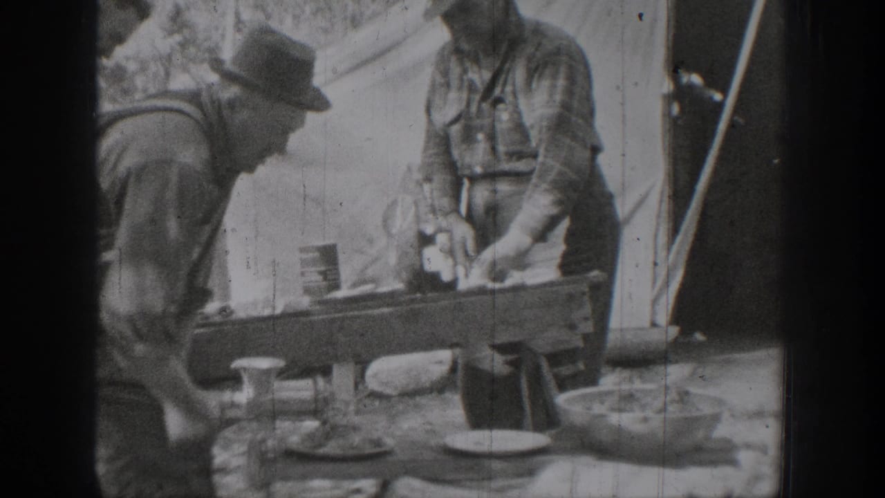 Two men prepare food or materials at a makeshift outdoor table beside a tent in the Chelan, Washington 1939 footage.
