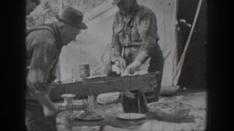 Two men prepare food or materials at a makeshift outdoor table beside a tent in the Chelan, Washington 1939 footage.