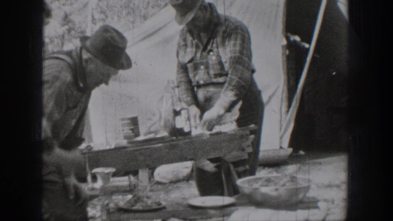 The home movie shows two men beside a tent using a tabletop hand-cranked device with bowls and cups nearby.
