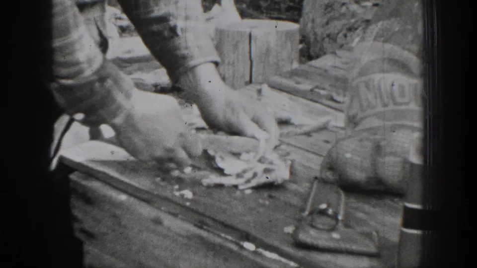 Close home-movie view of hands cutting or handling meat on a wooden outdoor table in the Chelan, Washington meat-preparation scene.