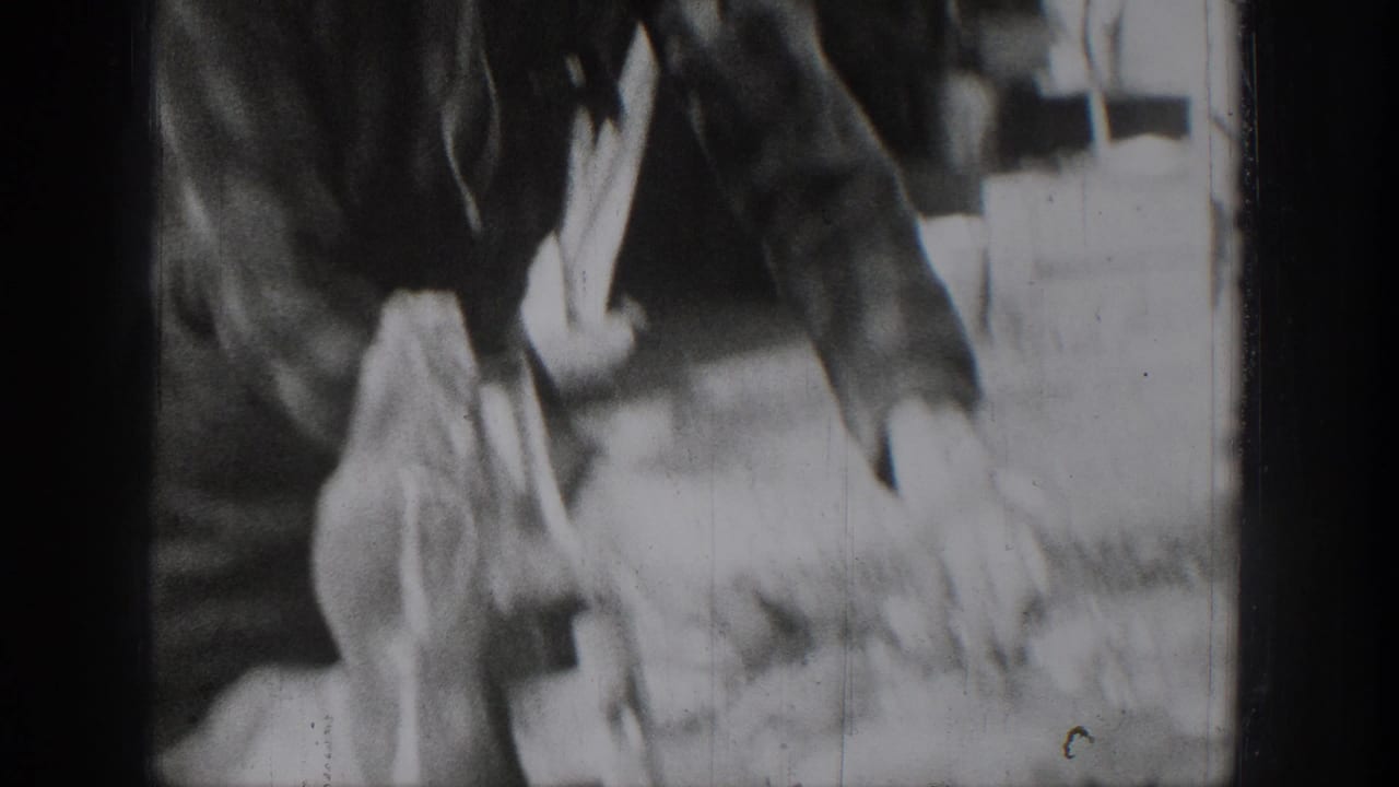 A person in dark period clothing bends over the outdoor food-preparation area in the Chelan home-movie footage.