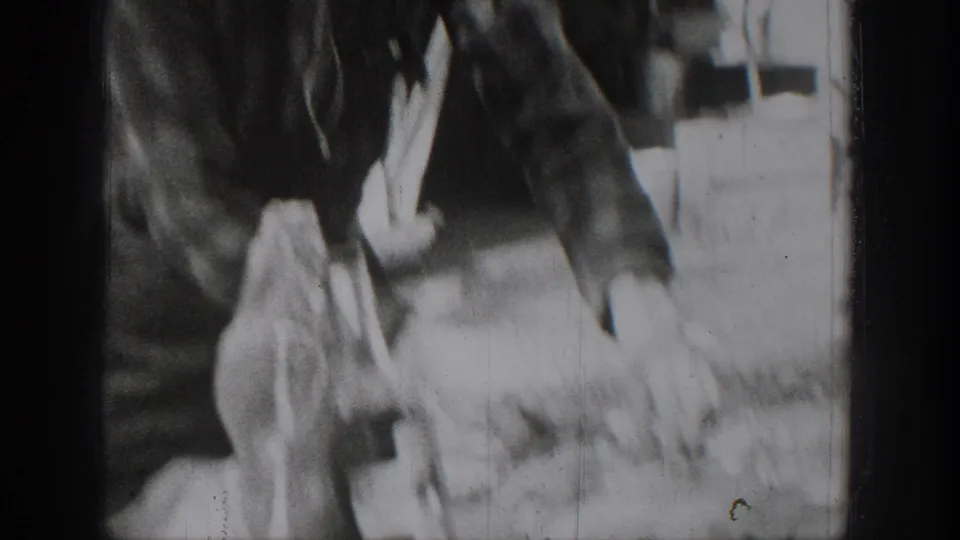 A person in dark period clothing bends over the outdoor food-preparation area in the Chelan home-movie footage.