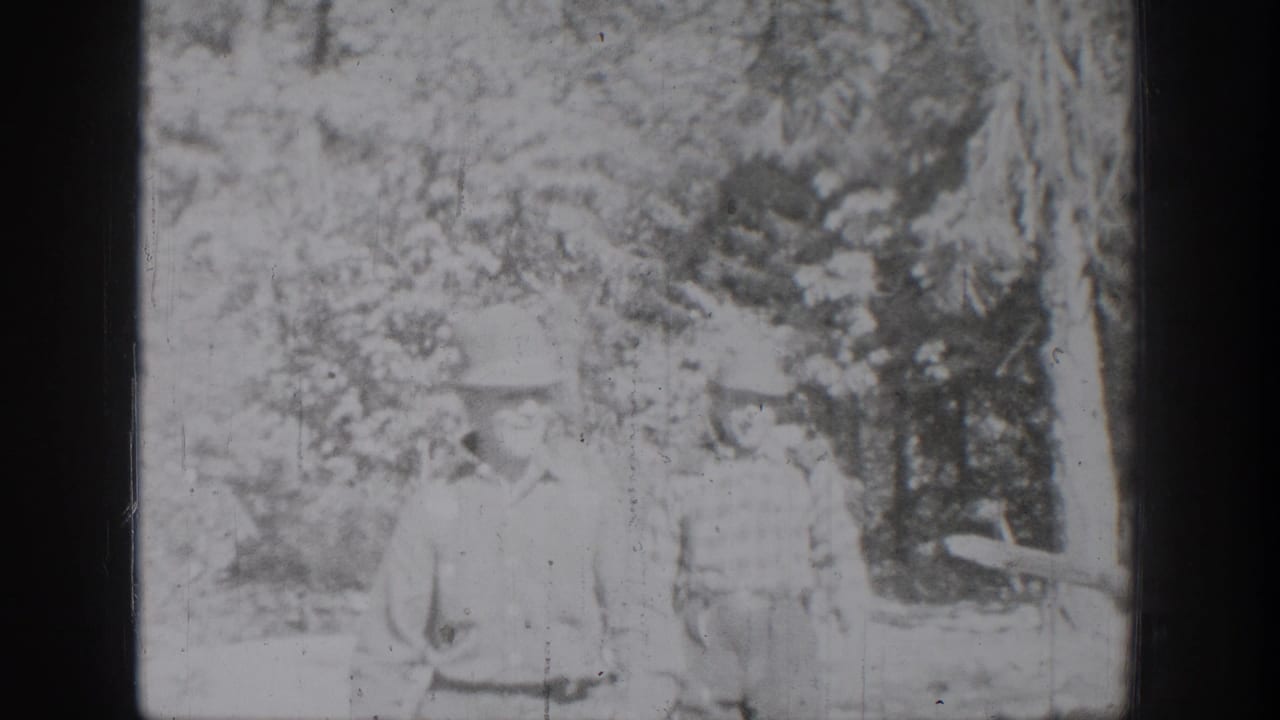 Chelan-area 1939 home-movie frame with two distant figures in light clothing among trees and soft overexposed foliage.