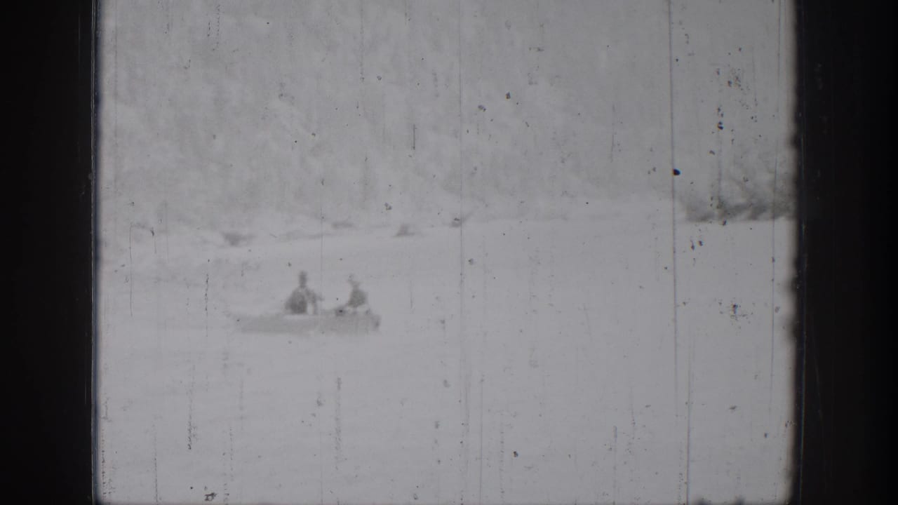 1939 Chelan home-movie frame showing two distant figures in a small boat against a bright lake and soft shoreline.