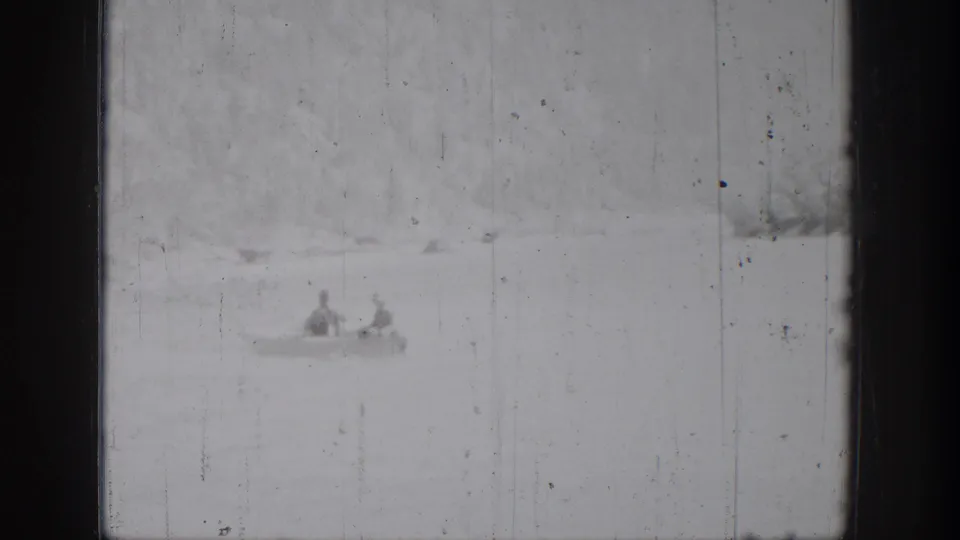 1939 Chelan home-movie frame showing two distant figures in a small boat against a bright lake and soft shoreline.