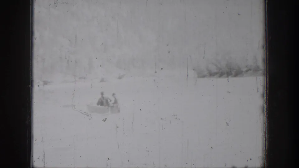 Two canoeists appear low in the frame on Lake Chelan, with a soft shoreline and visible 8mm scratches from the 1939 home movie.
