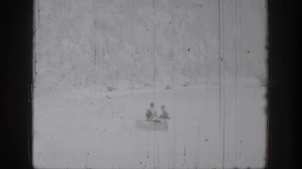Two men appear in a distant rowboat on Chelan lake water in 1939 black-and-white 8mm footage, with soft focus and scratches.