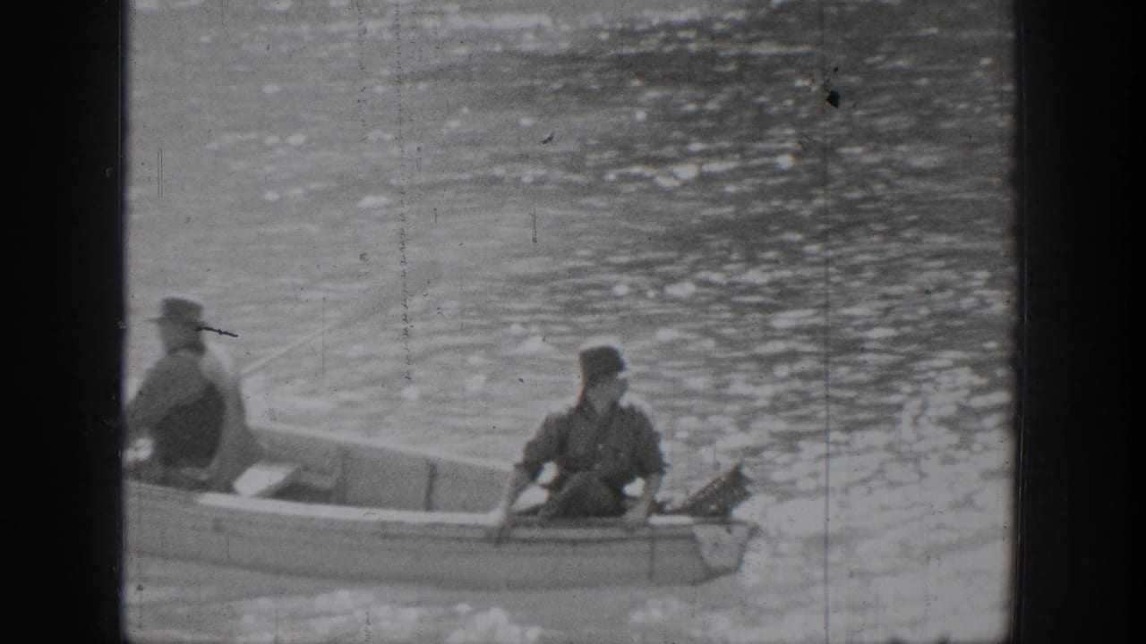 Closer 1939 Chelan frame of two men in a small rowboat on rippled lake water, one in a hat and one seated near the stern.