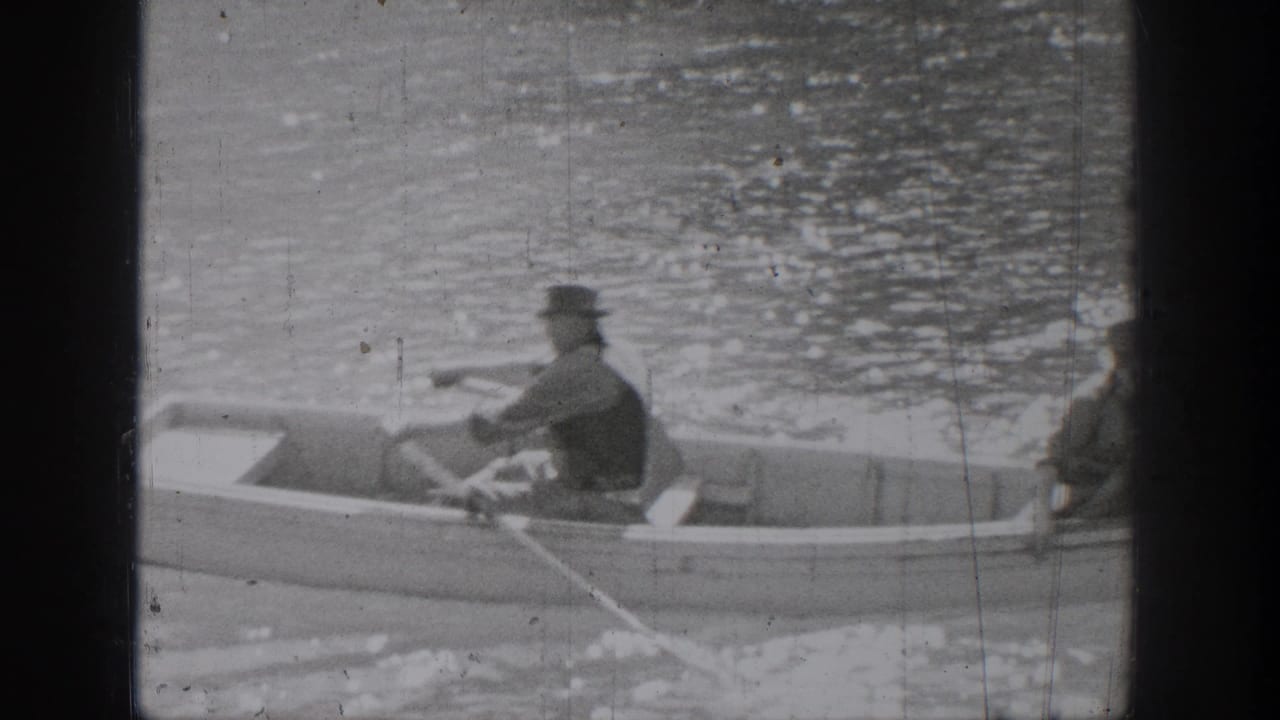 A man rows while another man sits near the edge of the rowboat.