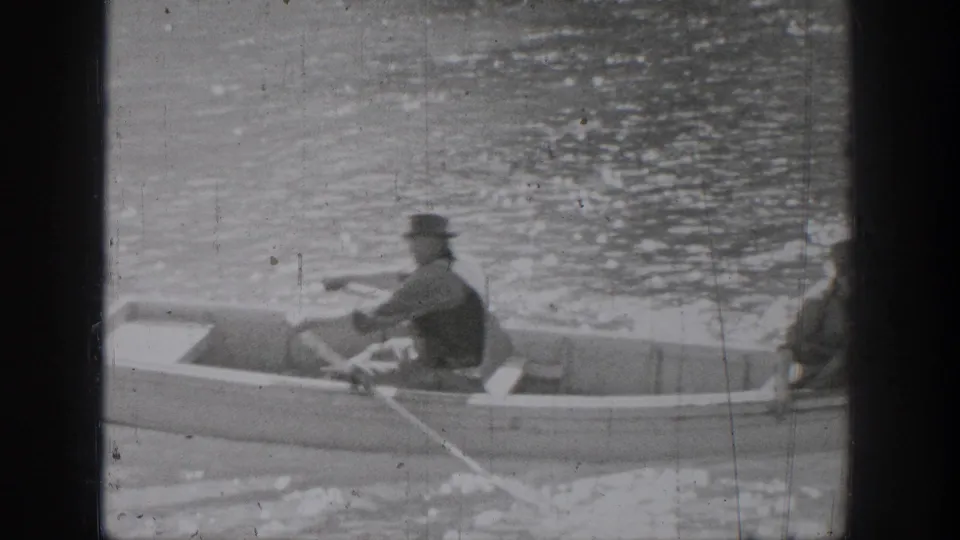 A 1939 Chelan home-movie frame shows one man rowing a small boat while another sits nearby on the water.
