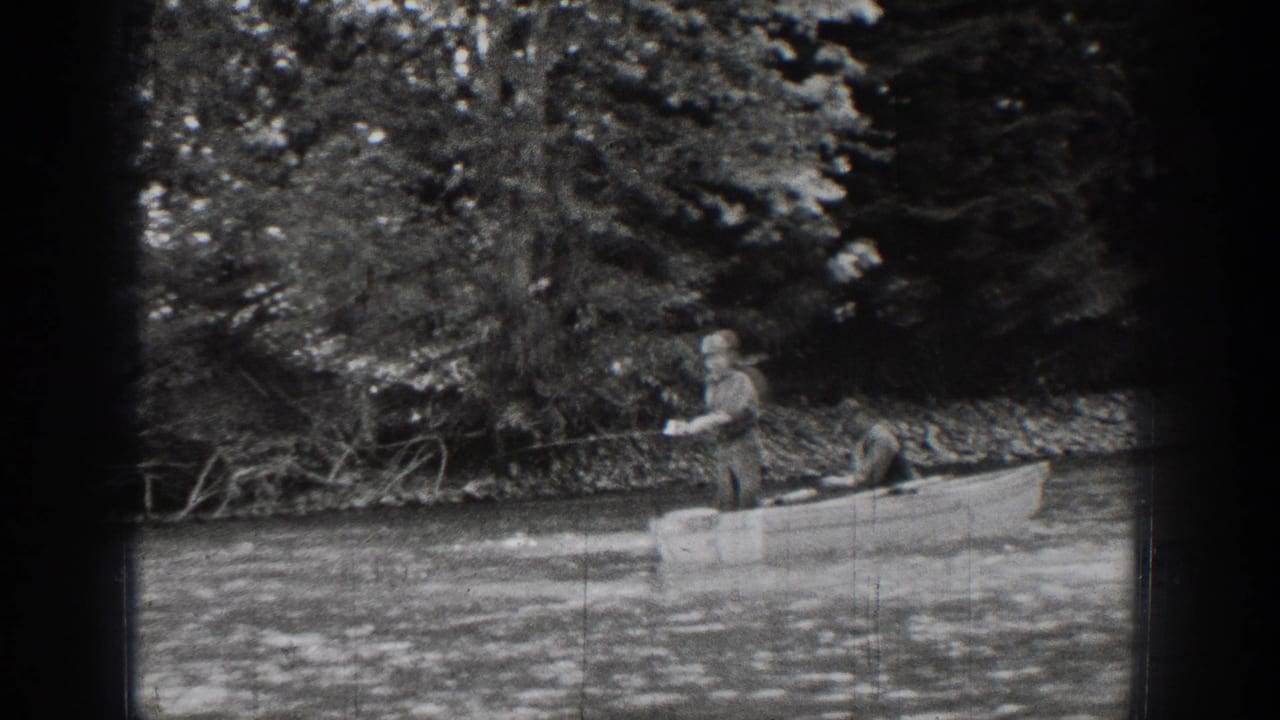 In Chelan, Washington, a man stands in a small boat on calm water beside dense trees in 1939 home-movie footage.