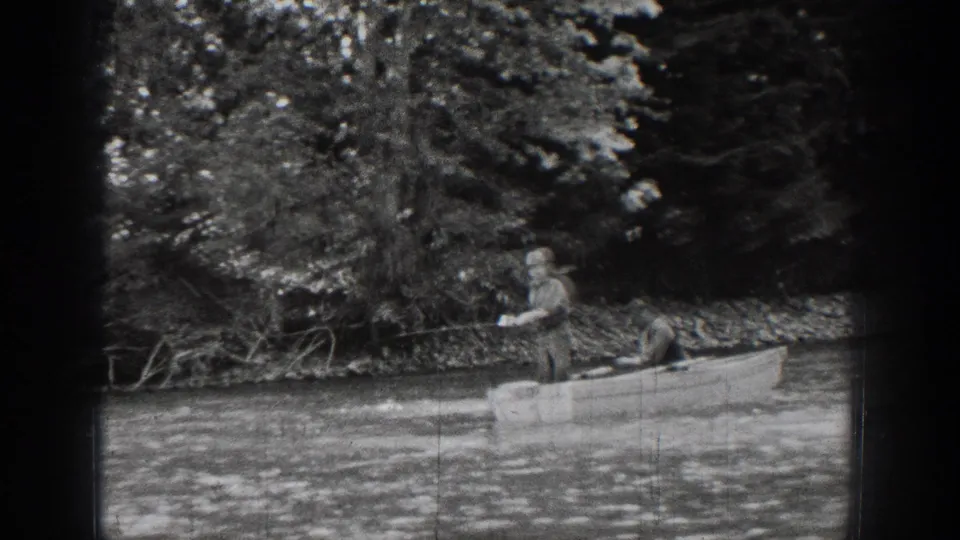 In Chelan, Washington, a man stands in a small boat on calm water beside dense trees in 1939 home-movie footage.