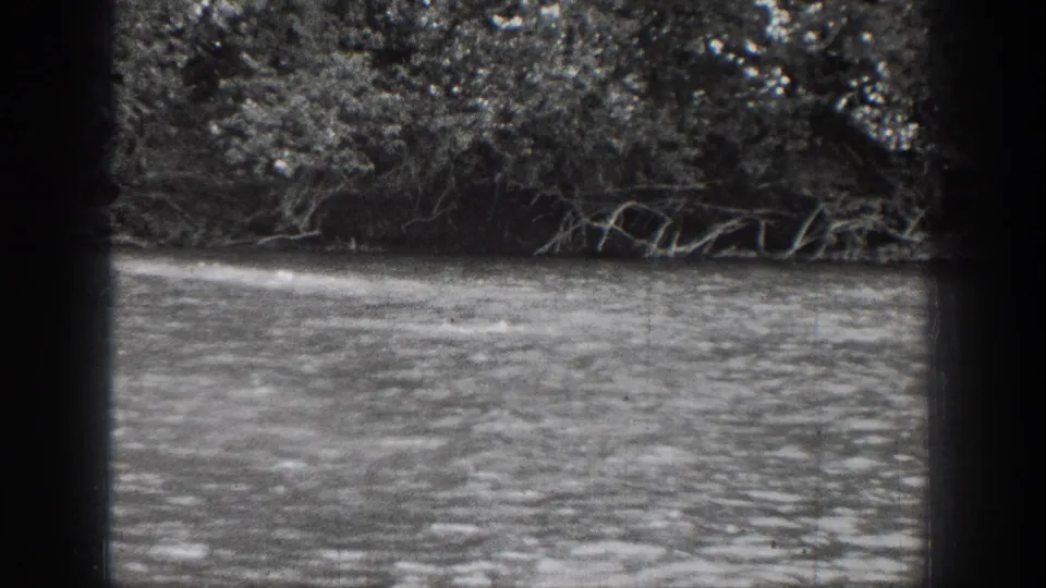 1939 Chelan, Washington home-movie frame showing rippled river water, dense trees, and overhanging branches along the far bank.