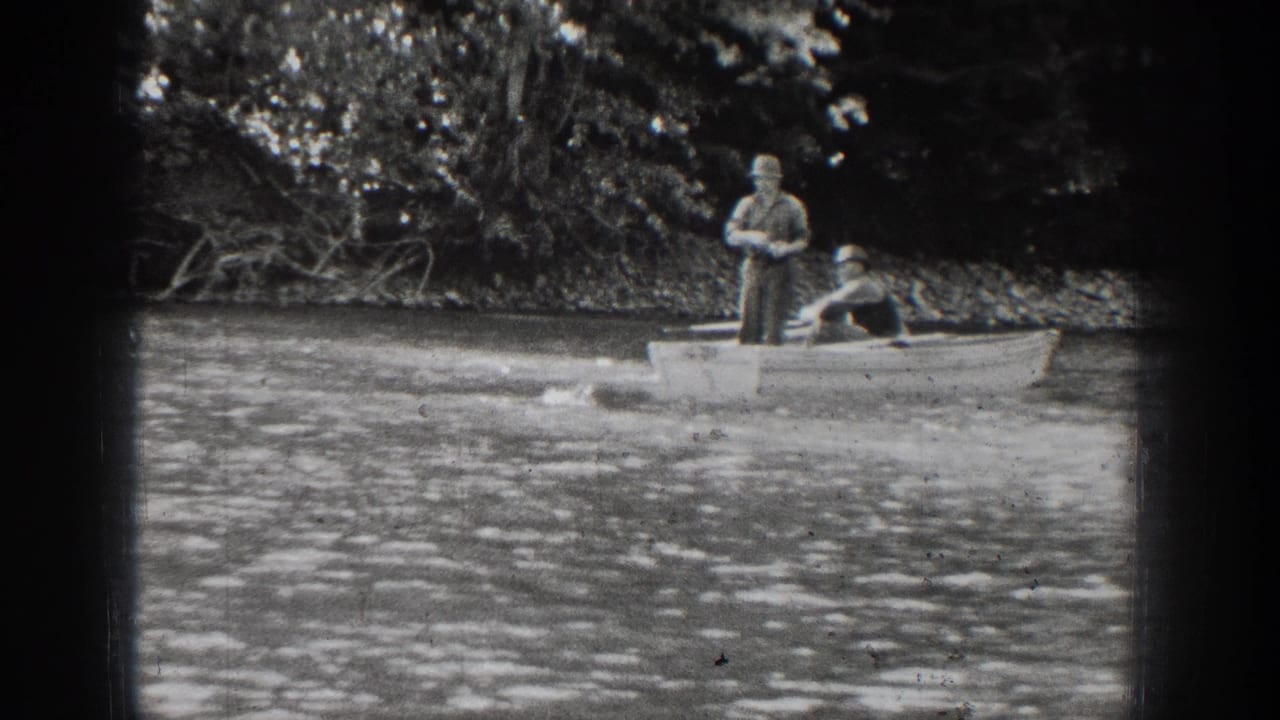 Two men in a rowboat on a lake, with one standing and one seated near the stern.