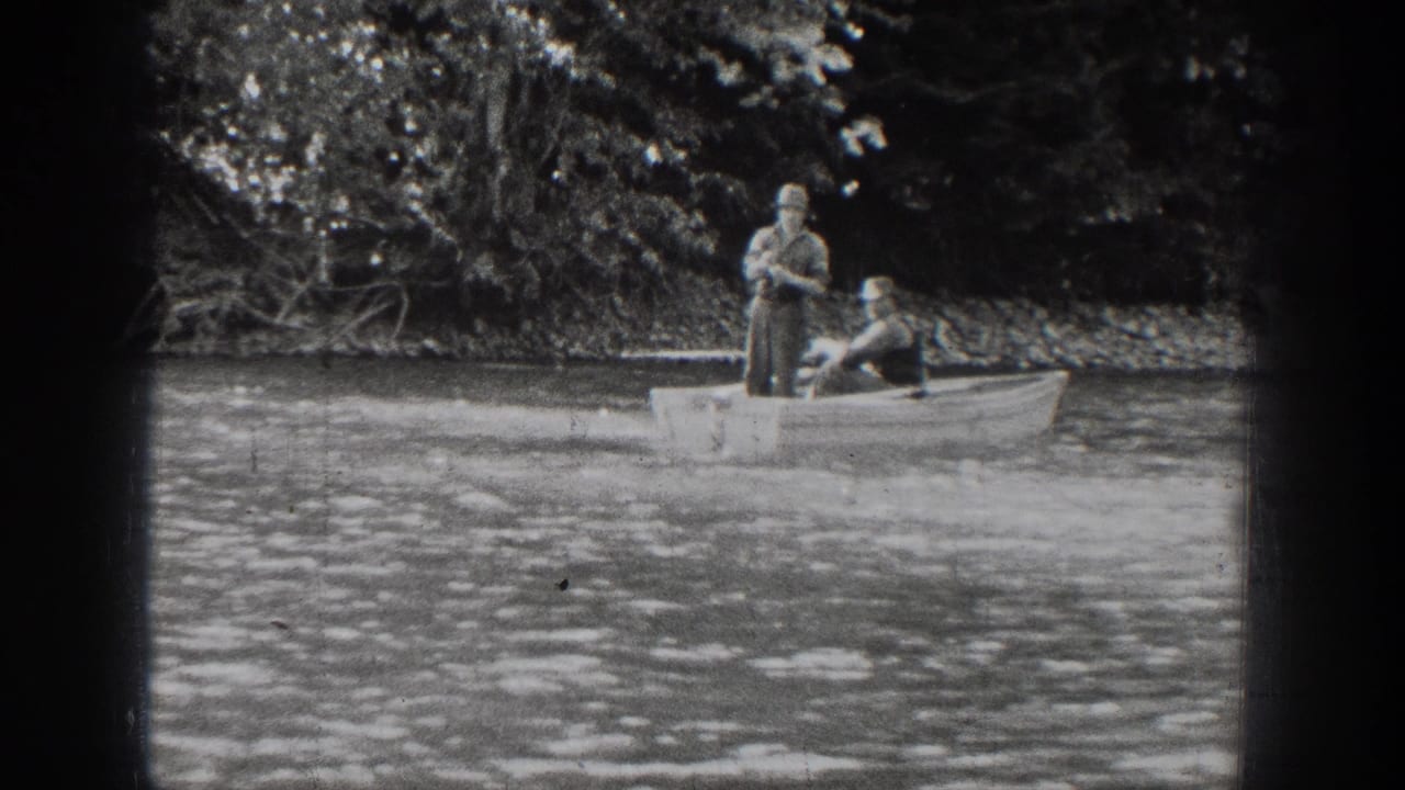 Two men continue fishing from a small rowboat on Lake Chelan, with the standing man handling the rod.