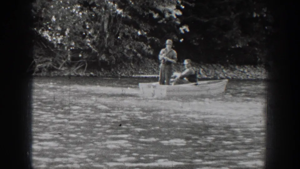 Two men continue fishing from a small rowboat on Lake Chelan, with the standing man handling the rod.