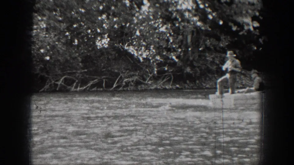 Chelan home-movie frame with a fisherman standing in a rowboat as the boat moves toward the edge of the frame.