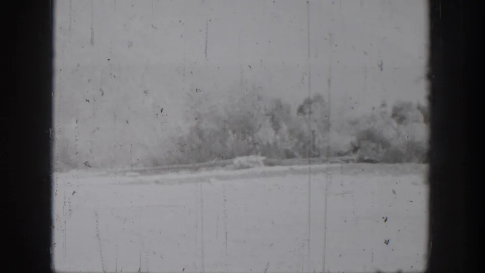 A blurry 1939 Chelan home-movie frame showing riverbank brush across calm water with scratches and dust on the film.