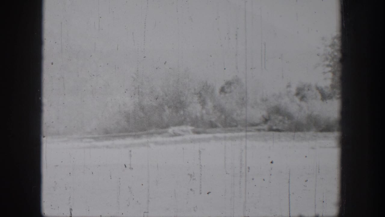 Chelan, Washington home-movie frame showing calm lake water and a distant wooded shoreline in soft black-and-white 8mm footage.