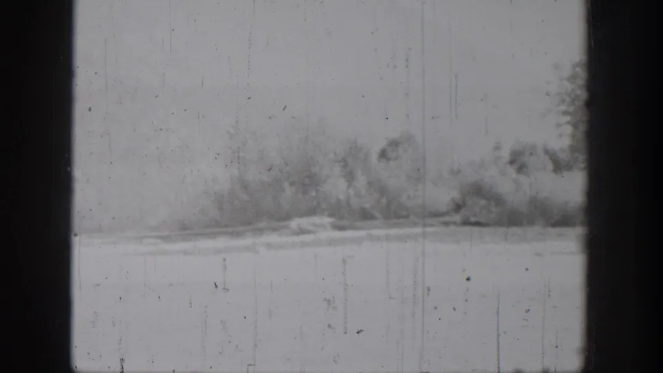 Chelan, Washington home-movie frame showing calm lake water and a distant wooded shoreline in soft black-and-white 8mm footage.